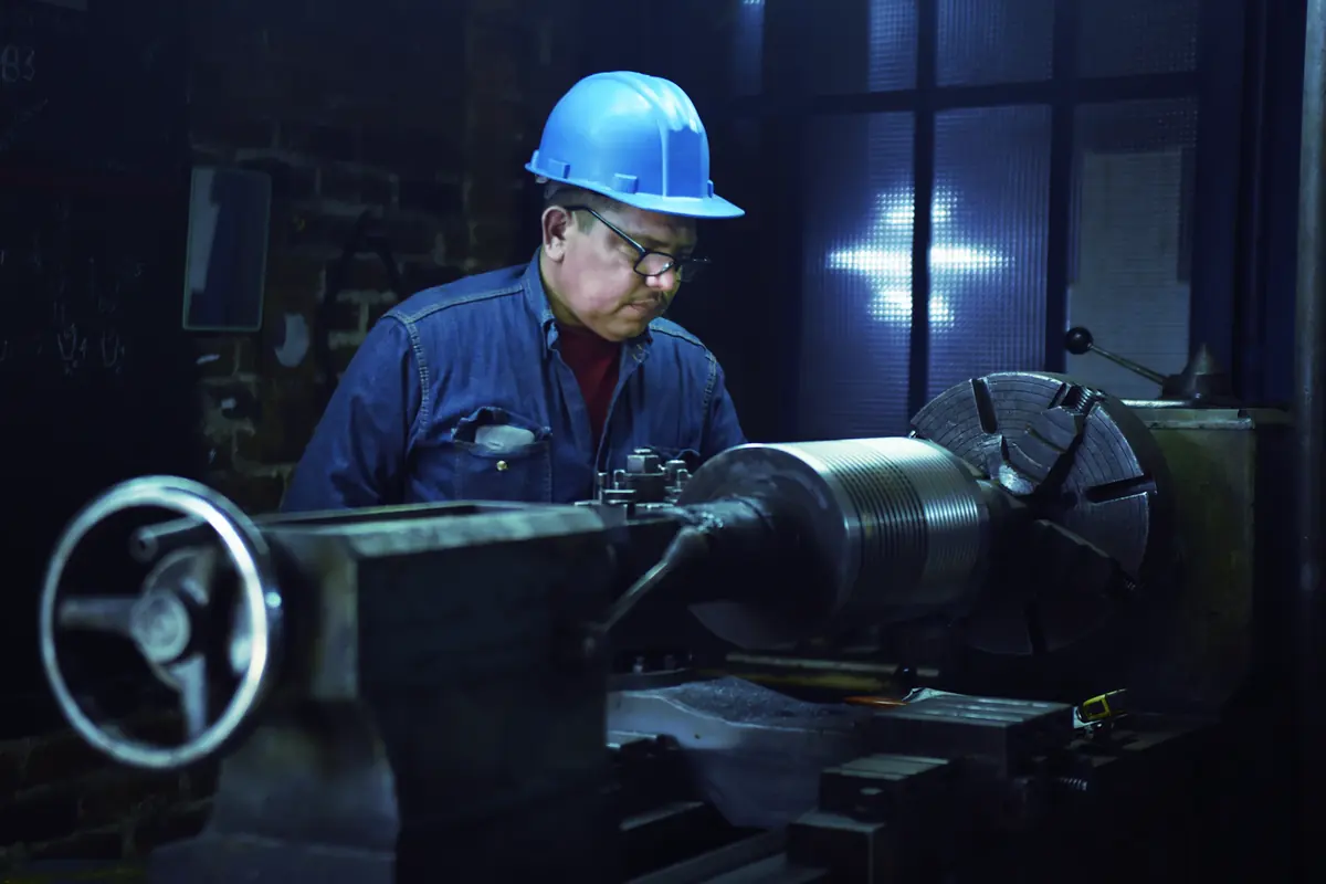 Trabajador con casco opera un torno en un taller industrial